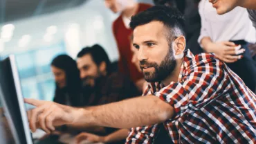 Personas colaborando frente a una computadora en una oficina moderna.