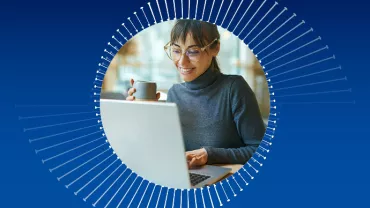 Persona trabajando en una computadora portátil con una taza en la mano.