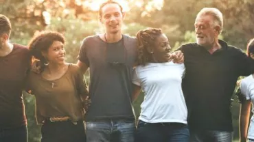 Grupo diverso de personas al aire libre, sonriendo y abrazándose al atardecer.