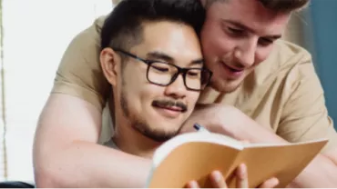 Dos personas leyendo un libro juntas en una habitación luminosa.