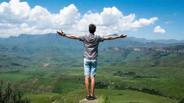 Persona en la cima de una montaña con los brazos abiertos hacia el paisaje.