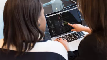 Dos personas revisan código en una computadora portátil.