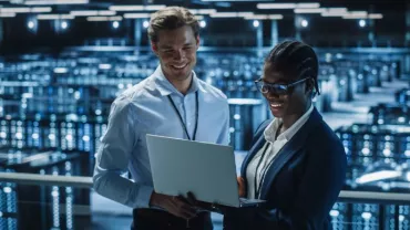 Dos personas miran una computadora portátil en un centro de datos iluminado.