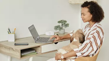 Persona trabajando en computadora portátil con un perro en brazos.