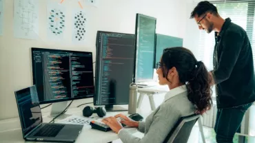 Personas trabajando en programación con varios monitores en una oficina.