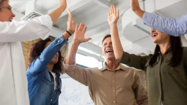 Trabajadores en círculo apoyándose y saludándose unos a otros con caras de felicidad.