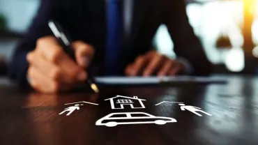 Persona escribiendo con íconos de casa, coche y personas sobre la mesa.