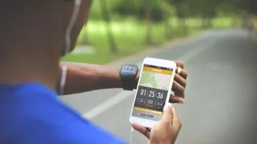 Persona usando una aplicación de ejercicio en el teléfono y un reloj inteligente en un camino.