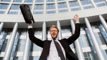 Persona vestida formalmente celebrando frente a un edificio de oficinas.