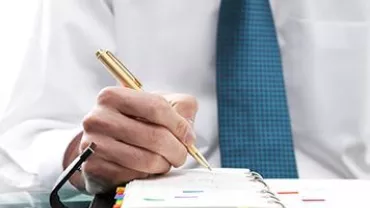 Persona usando una pluma dorada para escribir en una agenda.