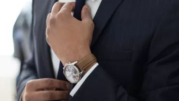 Persona ajustando una corbata y llevando reloj mientras lleva un traje.