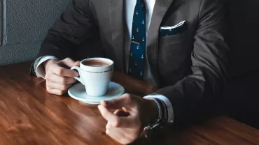 Persona en traje bebiendo café en una mesa de madera.