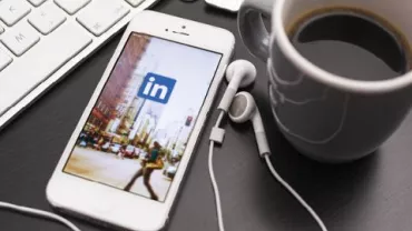 Teléfono con auriculares, logo de LinkedIn en pantalla y taza de café.